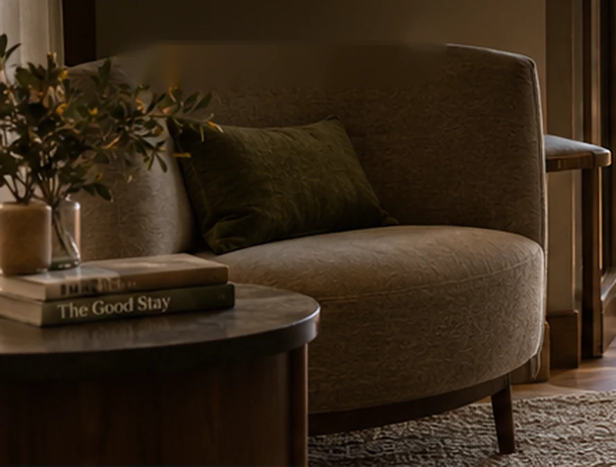 An olive green armchair next to a round wooden table with two books